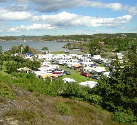 Bild av Malö Camping med en kustlinje i bakgrunden. Tält placerade vid en vik, omgivna av gröna träd och vatten. En husbil står parkerad nära campingen. Det ser ut som en idyllisk plats för naturälskare nära en resortstad.