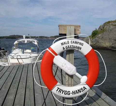 En motorbåt förtöjd vid en brygga med en livboj i förgrunden, omringad av andra båttillbehör. I bakgrunden syns det öppna vattnet och himlen.