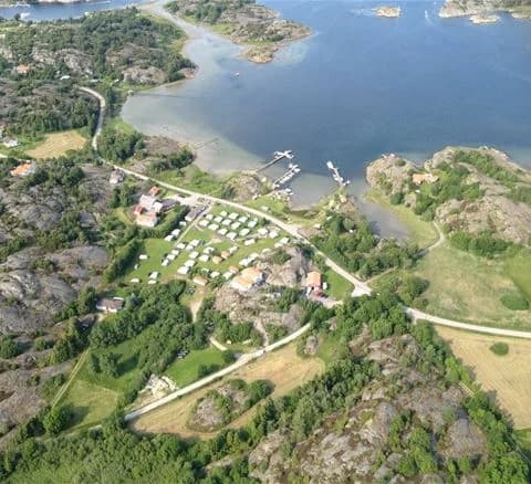 Flygfoto över Malö Camping visar ett naturskönt kustlandskap med campingplatser nära havet, en liten by och en vik omgiven av grönska och landsbygdsområden.