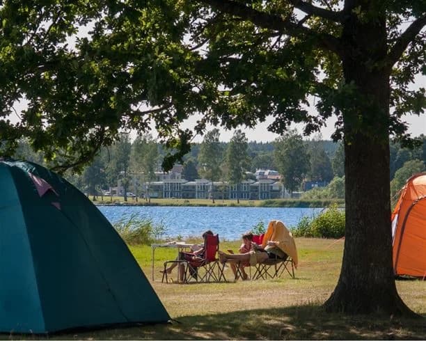 En somrig vy från Hultsfred strandcamping med tält uppställda nära kusten. På stranden finns utemöbler för avkoppling i skuggan.