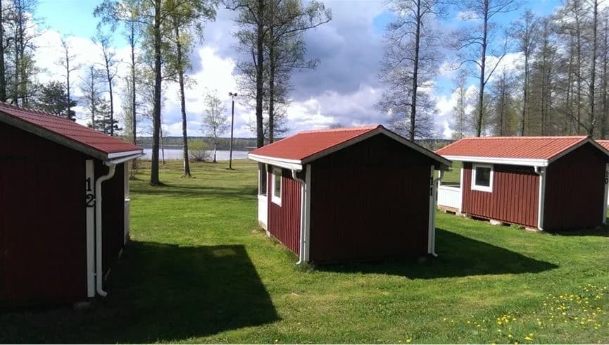 En pittoresk stuga med träfasad placerad på en välskött gräsmatta vid hultsfred strandcamping, omgiven av trädgårdsbyggnader och lummiga trädgårdar.
