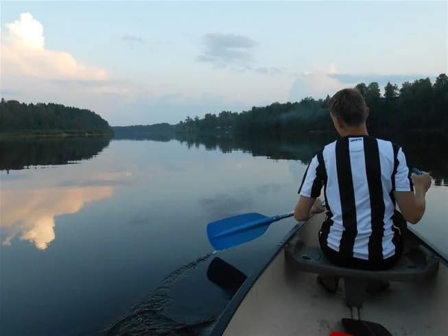 En stillsam sjö med flera roddbåtar som ligger vid en brygga vid Storängens camping, omgiven av lummig grönska och spegelblankt vatten, perfekt för friluftsaktiviteter och rekreation.