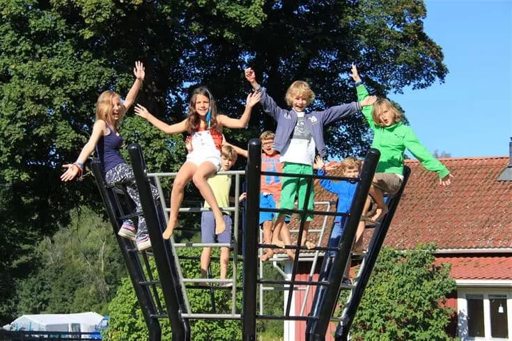 En grupp glada människor som njuter av sommaren på storängens camping. De deltar i utomhusaktiviteter och ser avslappnade ut i en solen i en skogsmiljö. En känsla av samhörighet och fritid utstrålas i den natursköna omgivningen.