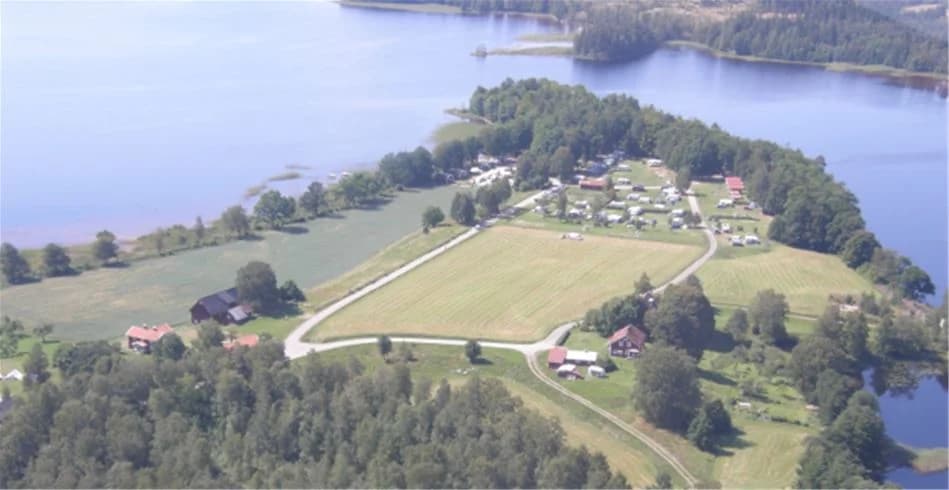 Fågelperspektiv över Vallsnäs Camping, med en vy över stugor, grönskande gräsmattor och en närliggande sjö som präglar det natursköna området.