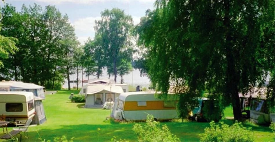 En campingplats i Vallsnäs med grönskande gräsmattor och parkområde. Flera husbilar och husvagnar är uppställda, och parasoller ger skugga åt besökarna.