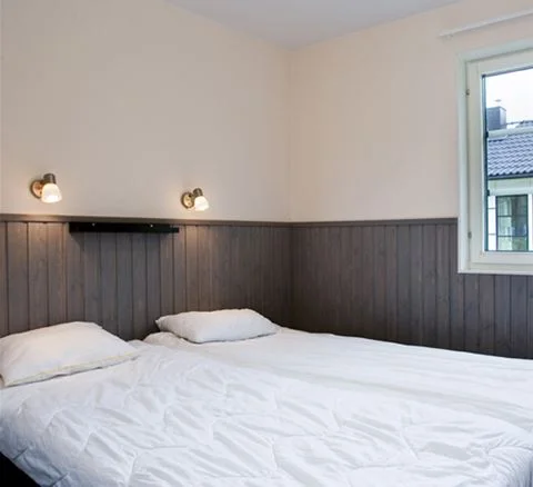 Sovrum på Gustavsvik Resort med träinspirerad inredning, en bekväm dubbelsäng med gråa sängkläder på ett trägolv.