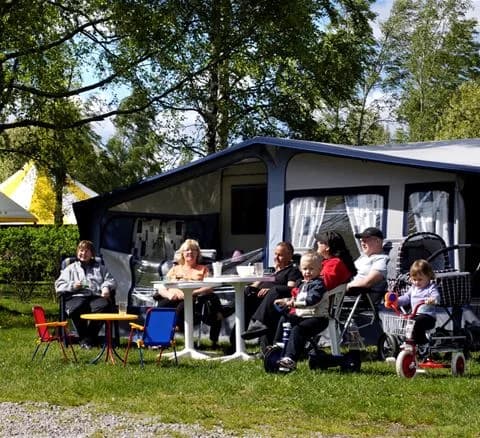 En bild från Gustavsvik Resort som visar en campingplats med tält och solstolar på en grönskande gräsmatta, perfekt för avkoppling och fritidsaktiviteter under semestern.