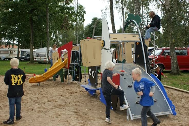 En barnvänlig lekplats med gungor och klätterställningar i en skuggig park på Jägersbo Camping Swecamp, perfekt för utomhuslek och rekreation.