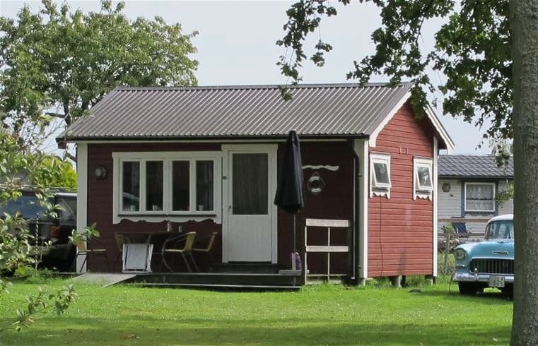 En liten stuga med rött tak och vita väggar på Jägersbo Camping, omgiven av grön gräsmatta och träd.