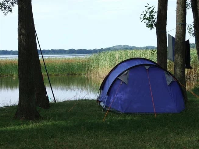 En tältplats vid Jägersbo Camping Swecamp med utsikt över en sjö omgiven av skogs- och våtmarkslandskap.
