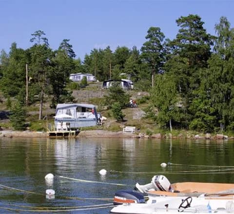 En pittoresk kustscen vid Hallmare Havsbad med båtar förtöjda längs strandkanten, omgivna av skimrande vatten och naturliga landformer.