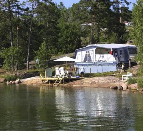 Bild av Hallmare Havsbad med en vacker kustlinje där stranden möter det lugna blå vattnet. I bakgrunden syns en båt på sjön och natursköna omgivningar med grönska. Perfekt plats för besökare som älskar natur och friluftsliv.