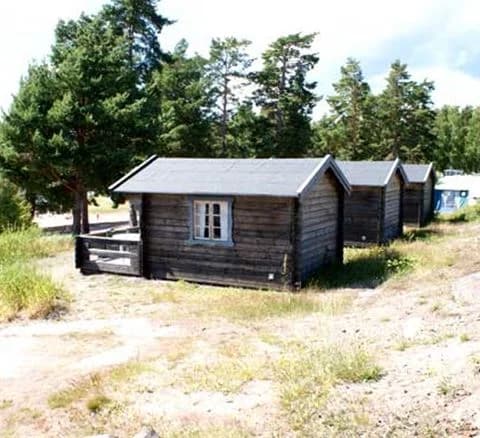 En liten stuga med träfasad och sadeltak står på en tomt vid Hallmare Havsbad. Omkring stugan finns en grönskande natur med träd och buskar som ger en pittoresk och fridfull atmosfär.