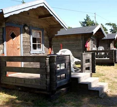 En mysig stuga med träfasad ligger omgiven av grönska vid Hallmare Havsbad. Utanför finns enkla utemöbler placerade på den välskötta gräsmattan.