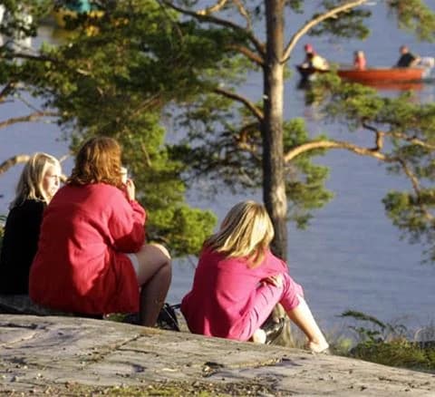 En solig sommardag vid Hallmare havsbad med människor som njuter av stranden och badar i sjön.