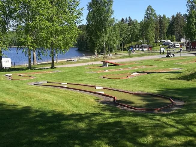 En lummig parkmiljö vid Degernäs Camping, med grönskande gräsmattor, stigar och flera picnicbord och bänkar för avkoppling och rekreation.