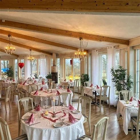 En matsalsmiljö med bord klädda med dukar och stolar runt omkring. Flera bord är uppställda i ett rum som kan vara en del av en restaurang på Degernäs camping. Det syns takdetaljer och inredningen ger en inblick i ett mysigt matställe.