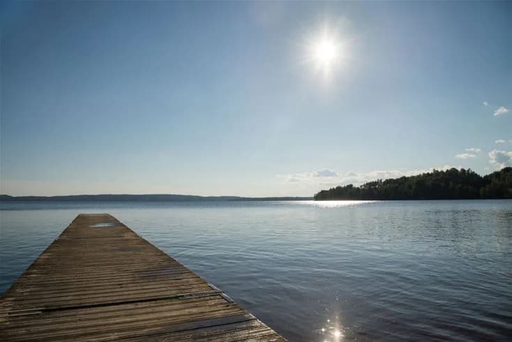 Vid Sandaholm restaurang & camping sträcker sig ett blått, rofyllt vatten ut mot horisonten, krönt av en klar himmel, vilket skapar en fridfull och inbjudande atmosfär.