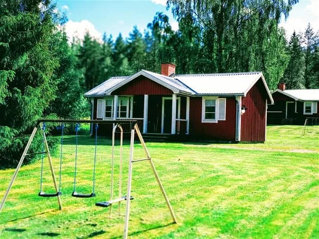 En stuga med rött tak omgiven av en grön gräsmatta i ett lantligt område vid Sysslebäcks stugby & fiskecamping.