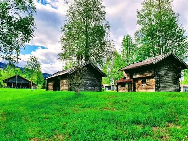 En grön och lantlig miljö med en liten stuga, omgiven av gräsmattor och träd på Sysslebäcks Stugby & Fiskecamping.
