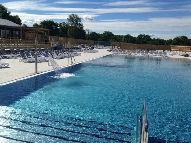 Alt-text: En översiktsbild av poolområdet på Lundegård Camping & Stugby, med en stor pool omgiven av solstolar och gröna träd, vilket skapar en inbjudande semesterkänsla.