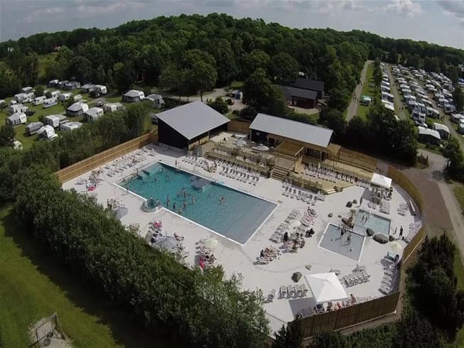 Fågelperspektiv av Lundegård Camping & Stugby, med en swimmingpool omgiven av gröna områden och stugor.