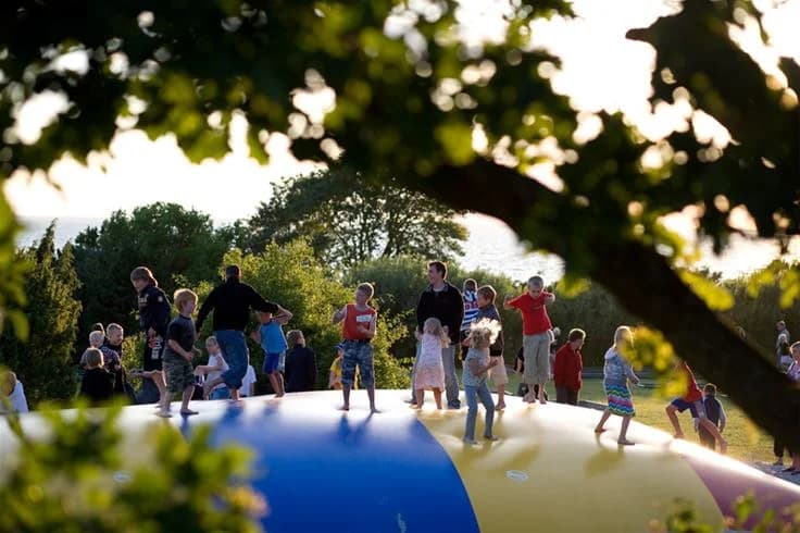 En sommardag på Lundegård Camping & Stugby med barn som leker på uppblåsbara lekredskap utomhus. Besökare njuter av rekreation och fritidsaktiviteter i den soliga, gröna naturen.