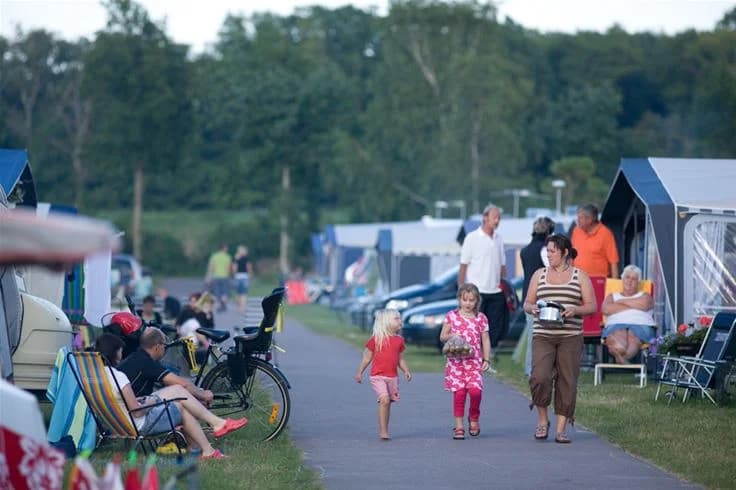En somrig campingplats på Lundegård Camping & Stugby med tält, stolar och picknickområde, omgiven av grönska och solig himmel, vilket skapar en avslappnad och rolig semesteratmosfär.