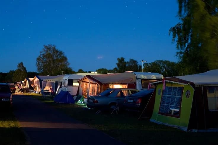 En campingplats på natten med tält och en bil omgiven av träd under en stjärnklar himmel på Lundegård Camping & Stugby.