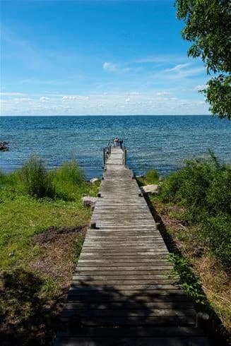 En träbrygga sträcker sig ut över ett blått hav under en klar sommarhimmel vid Lundegård camping & stugby.