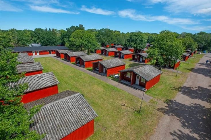 En vidsträckt gräsyta på Lundegård Camping & Stugby, omgiven av träd och buskar, med en klar himmel ovanför, som inbjuder till utomhusaktiviteter och avkoppling.