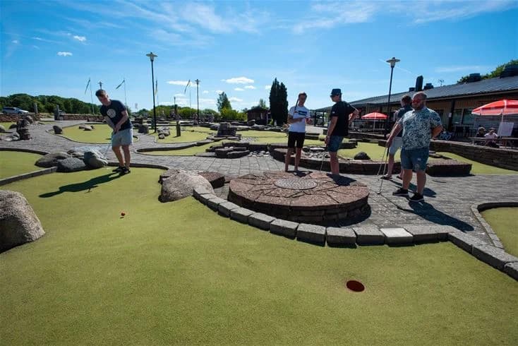 En livlig campingmiljö med besökare som spelar minigolf. Grönskande omgivningar med lekfulla inslag och en familjevänlig atmosfär.