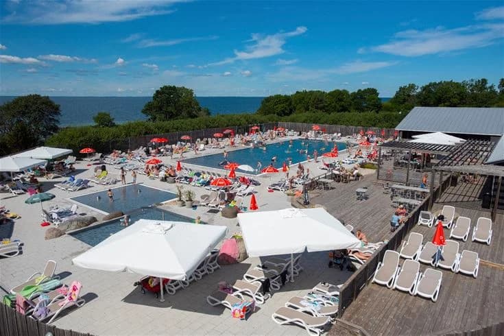 Bild av lundegård camping & stugby: En utomhuspool omgiven av solstolar och utemöbler. Människor njuter av soligt väder och avkoppling, vilket skapar en semesterkänsla på campingen.