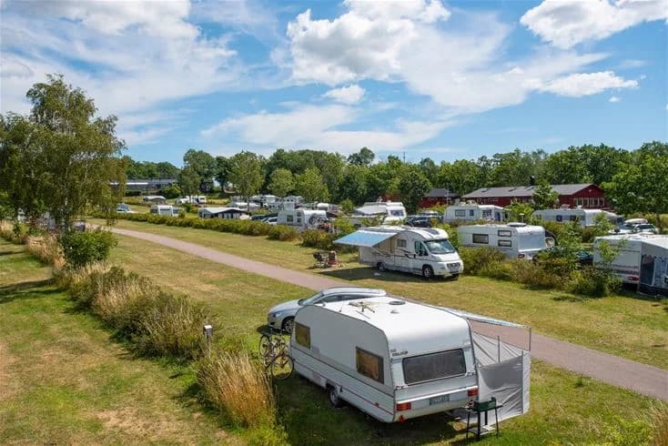 En stor campingplats vid Lundegård Camping & Stugby med husbilar och husvagnar parkerade i rader, omgivet av grönska och en klar himmel.