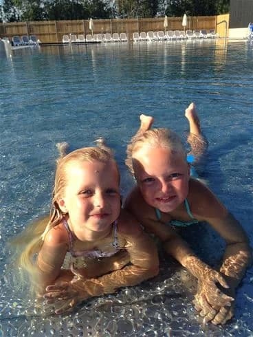 En glad familj njuter av sommarledigheten på Lundegård Camping & Stugby. De ler och har roligt tillsammans i den soliga utomhusmiljön.