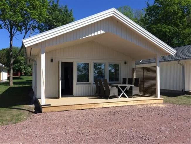 Lundegård Camping & Stugby: En skuggig uteplats med träkonstruktion och trästaket, omgiven av lövträ och en välskött gårdsplan.