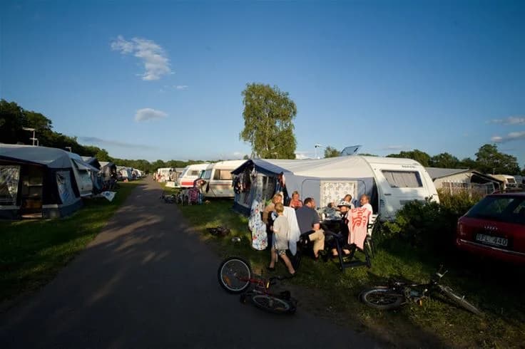 En bild som visar en campingplats på Lundegård camping & stugby, med flera husvagnar uppställda på en gräsyta. Området ser ut att vara en populär semesterdestination med besökare som njuter av utomhusaktiviteter.