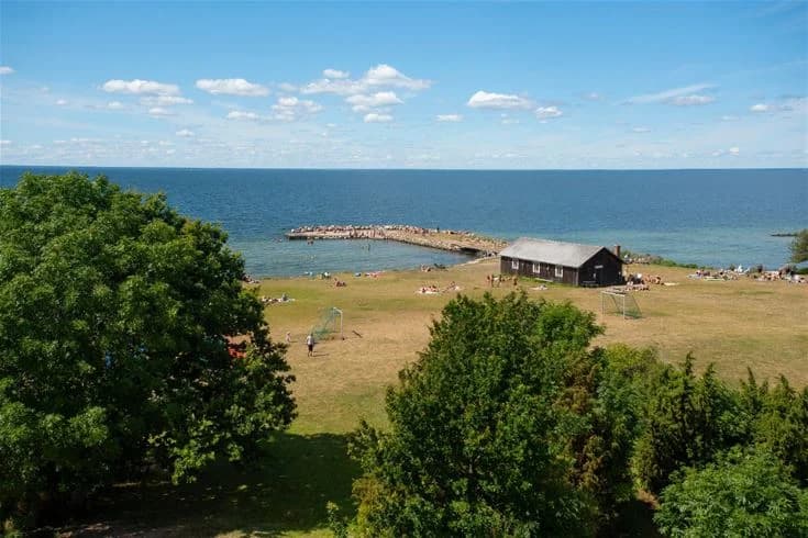 Vy över en somrig kustlinje vid Lundegård Camping & Stugby, med ett klart hav som sträcker sig mot horisonten och en sandstrand i förgrunden.