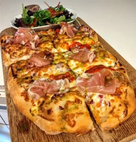 En närbild av en nygräddad pizza på Lundegård Camping & Stugby, fylld med ost, charkuterier och andra smakrika ingredienser.