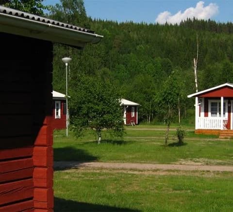 Bild av Klarälvens camping med en stuga på en grön gräsmatta omgiven av öppna landskap. Stugan ligger i ett lantligt område och omges av en välskött trädgård.