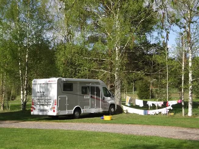 En husvagn och en skåpbil parkerade vid en campingplats i Tiveden, omgivna av grönska och öppna ytor för fritidsaktiviteter.