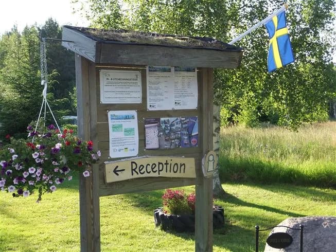 Alt-text: En grönskande campingplats i Tiveden med gräsytor, växter och rekreationsområden, omgiven av en lummig trädgårdsmiljö.
