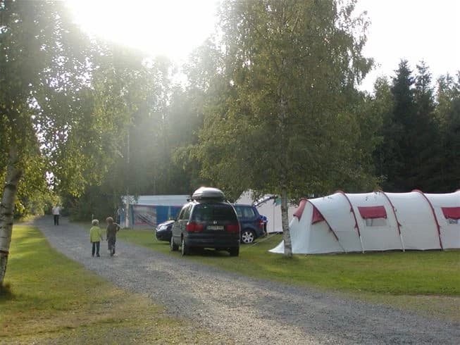 En campingplats i Tiveden med tält och husbilar parkerade på gräsytan under blå himmel.