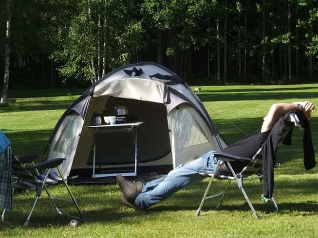 En tältplats på Camping Tiveden, med ett tält och ryggsäckar omgivna av skog och natur, förmedlar en känsla av friluftsliv och avkoppling.