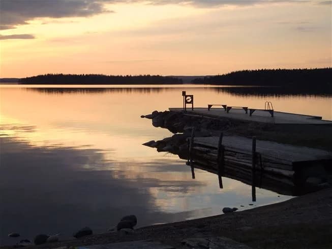 En stilla sjö vid skymningen, med en färgrik solnedgång vid horisonten.
