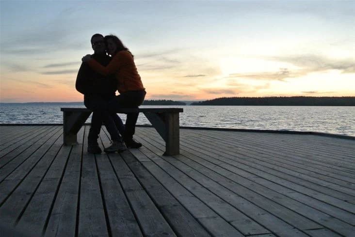 En romantisk solnedgång över en stilla sjö vid Tivedens camping, med par som njuter av kvällen vid vattnet.