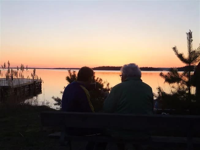 En vacker solnedgång över en lugn kustlinje vid camping Tiveden, med en himmel som skiftar i orange och rödtoner.
