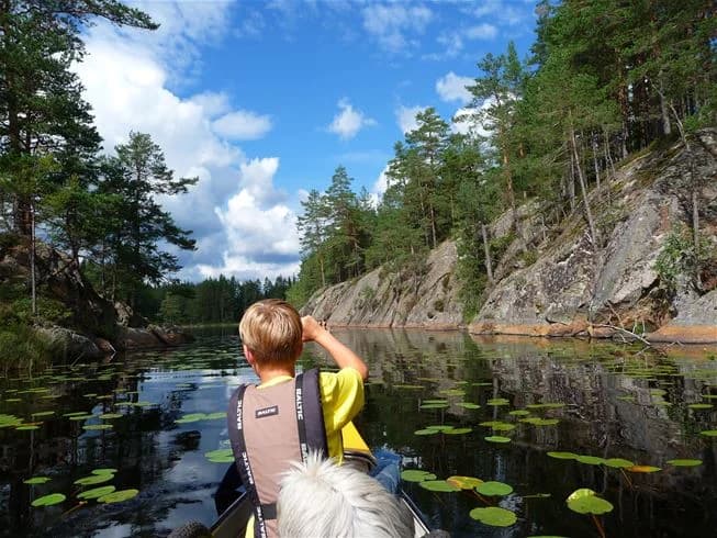 En liten båt flyter på ett stilla vattendrag omgiven av grönskande natur, som är en del av den natursköna campingplatsen i Tiveden.