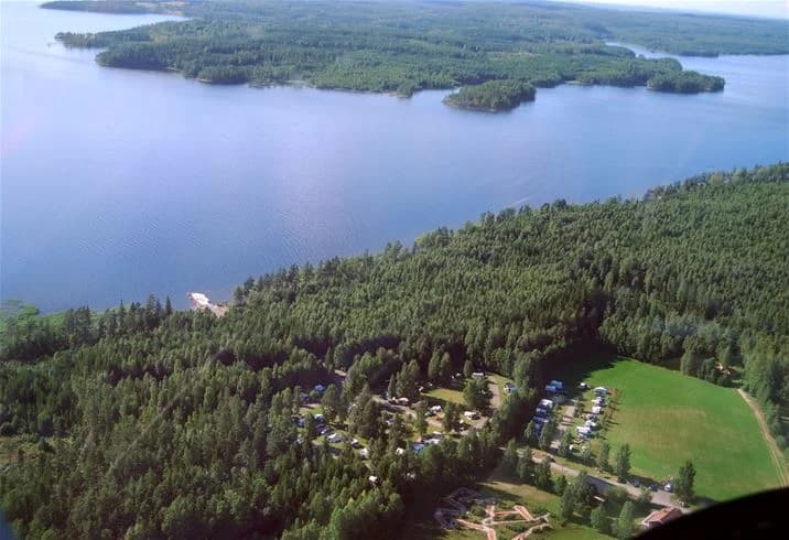 En fågelperspektivsbild som visar ett naturskönt område vid Camping Tiveden, med en vattenreservoar omgiven av frodig grönska och ett landskap präglat av vattenvägar och kustformer.