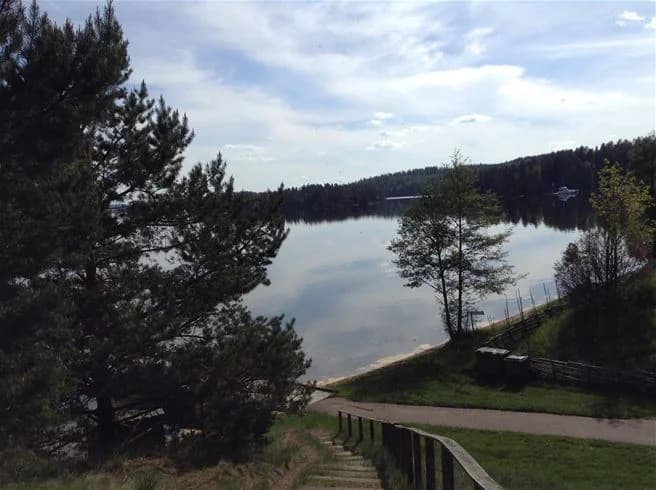 En naturskön vy över en sjö vid Malexander camping, omgiven av gröna sluttningar och klarblå himmel.